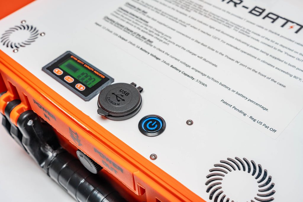 Close-up of an orange and white portable battery testing device with a digital display screen, USB port, and power button.
